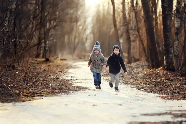 コートを着た2人の陽気な少年とデルジシーシャの手を走る歩道の帽子春 — ストック写真