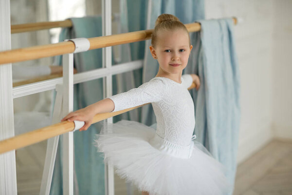 A little girl a ballerina in a white tutu and kitschka is busy at the bench. The concept of children and dance