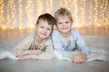 İki küçük çocuk Noel ışıklarının arka planında yerde yatıyor.