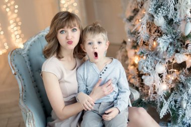 Noel ağacının yanında açık renk elbiseli iki küçük çocuk hediyeleri açıyor. Yeni Yıl