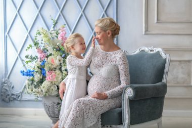 Dantel elbiseli, kızıyla birlikte sarışın hamile bir kadın.