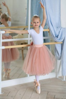 Pembe etekli güzel bir balerin bale sopasının yanında duruyor. Bale dersi. Çocuklar ve bale