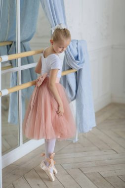 Pembe etekli güzel bir balerin bale sopasının yanında duruyor. Bale dersi. Çocuklar ve bale