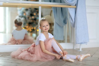 Pembe etekli güzel bir balerin bale sopasının yanında duruyor. Bale dersi. Çocuklar ve bale