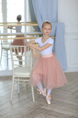 Pembe etekli güzel bir balerin bale sopasının yanında duruyor. Bale dersi. Çocuklar ve bale