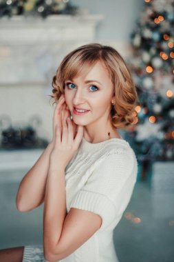 Noel ağacının yanında mavi gözlü beyaz elbiseli güzel bir kadının portresi.