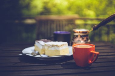 Kırsal kahvaltı. Kahve fincanlı ahşap kahve masası, Céve gölü kremalı pasta, lezzetli Slovenian tatlıları. Kremna Rezina veya Cremeschnitte