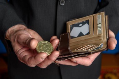 Takım elbiseli bir adam elinde Bitcoin ve cüzdan tutuyor..