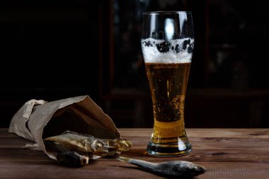 Tahta bir masada bir bardak bira ve kurutulmuş balık.