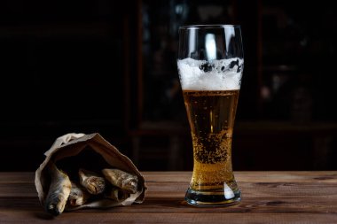 Tahta bir masada bir bardak bira ve kurutulmuş balık.