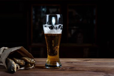 Tahta bir masada bir bardak bira ve kurutulmuş balık.