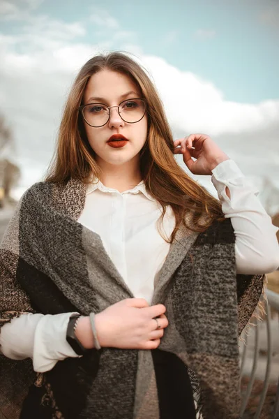 Una chica con gafas y una bufanda a cuadros en los hombros en la calle. — Foto de Stock