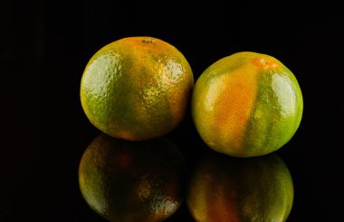 Siyah bir zemin üzerinde iki taze, olgun sarı-yeşil mandalina..