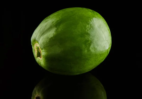 Papaya verde redonda sobre fondo negro con reflejo — Foto de Stock