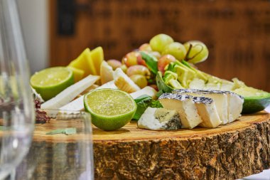 Üzüm, limon, ananas ve bitkilerle tahta bir tahtanın üzerinde seçilmiş peynirlerin dilimlenmesi