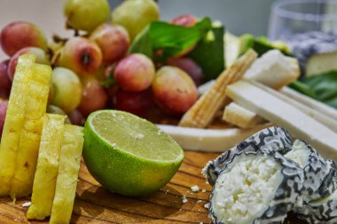 Üzüm, limon, ananas ve bitkilerle tahta bir tahtanın üzerinde seçilmiş peynirlerin dilimlenmesi