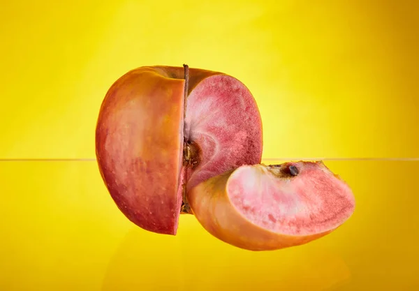 In der Nähe liegt ein Apfel mit rotem Fruchtfleisch im Schnittkeil. Gelber Hintergrund isoliert. Exotische Früchte, gesunde Ernährung — Stockfoto