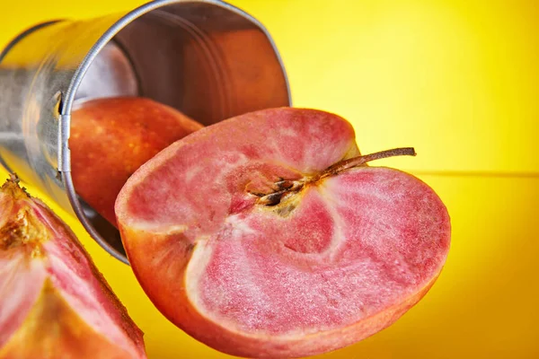 Une pomme avec de la pulpe rouge à l'intérieur avec un coin sculpté sur le fond d'un seau. Fond jaune isolé. Fruits exotiques, aliments sains — Photo