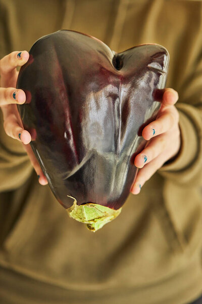 Ugly eggplant in the shape of a heart holds with two hands. Funny, abnormal vegetable or food waste concept