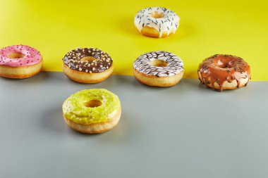 Çok renkli donutlar ve sarı-gri arka plan üzerine serpiştirilmiş jöleler..