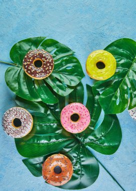 Renkli çörekler, krema serpiştirme mavi arka plandaki canavar yapraklarına serpiştirme..