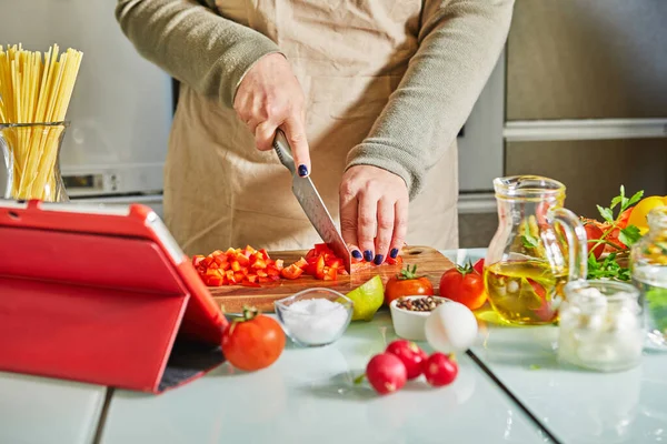 Online sanal uzmanlık kursuna göre yemek pişiren bir kadın ve dijital tarife bakıp evde mutfakta sağlıklı yemek pişirirken dokunmatik ekran tableti kullanan bir kadın..