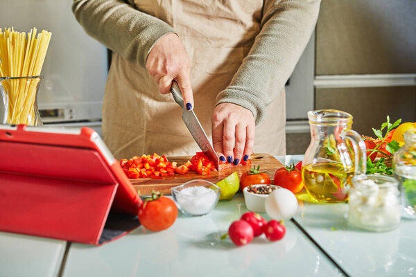 Woman cooking according the tutorial of online virtual master class, And looking on the digital recipe, using touchscreen tablet while cooking healthy meal on the kitchen at home.