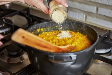 İnternetteki tariflere göre mutfakta yemek pişirmek. Kadın tavada risottoya parmesan ekliyor. Adım adım tarif.