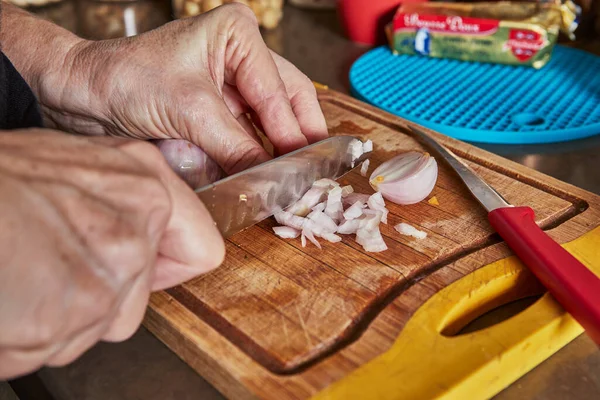 İnternetteki tariflere göre mutfakta yemek pişirmek. Kadın risotto yapmak için mini soğan kesiyor. Adım adım tarif.
