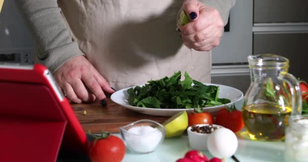 Mujer cocina de acuerdo con el tutorial de la clase magistral virtual en línea, y mirando la receta digital, utilizando la tableta de pantalla táctil mientras cocina comida saludable en la cocina en casa — Vídeo de stock