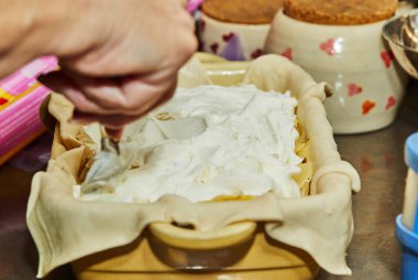 İnternetteki tariflere göre mutfakta yemek pişirmek. Kadın, soğanlı patates turtasına ekşi krema ekliyor. Adım adım tarif.