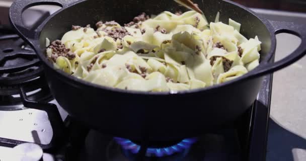 A darált húst egy serpenyőben megsütik tésztával a gázon, és fából készült spatulával keverik, hogy spagettit készítsenek. — Stock videók