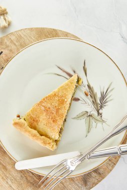 Bir dilim İsviçre turtası, pazı, pirinç, soğan ve çam fıstığı beyaz mermer üzerinde, tabakta duruyor. Düz yatıyordu