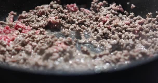 Gehakt vlees wordt gebakken in koekenpan op gas en geroerd met houten spatel om spaghetti bolognese te maken — Stockvideo