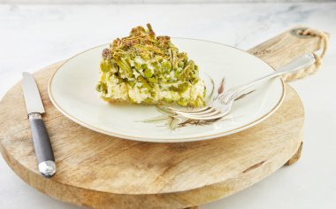 Kuşkonmazlı dilimlenmiş turta, tabak ve ahşap tezgahta bezelye. Adım adım tarif.