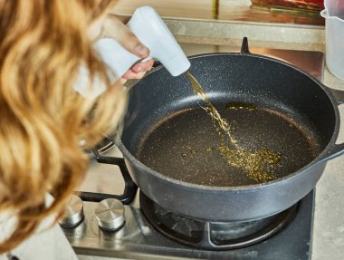 Teenager sprinkles sunflower oil in frying pan for making spaghetti bolognese using recipe from the Internet.