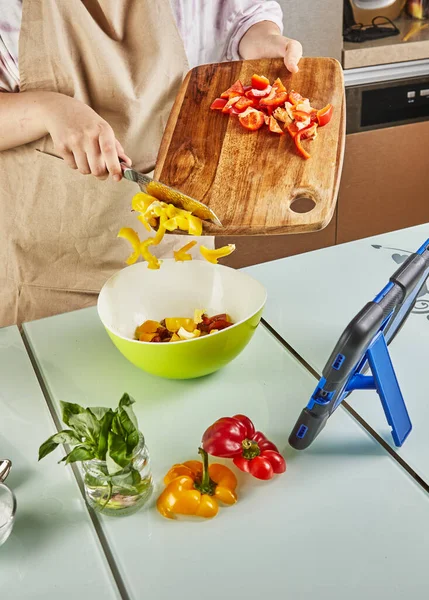 Ergen, çevrimiçi bir dersten salata hazırlıyor ve evde mutfakta sağlıklı yemek hazırlarken dokunma tabletinden dijital tarifi izliyor..