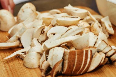 Kadın tahta kesme tahtasıyla mantar kesiyor. Mutfaktaki yemek tarifine göre pişiriyor.