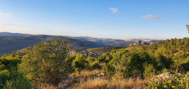 Yeşil vadilerin ve uzak şehir binalarının engin manzarası açık mavi gökyüzünün altında altın saatinde bir tepenin zirvesinden çekildi..