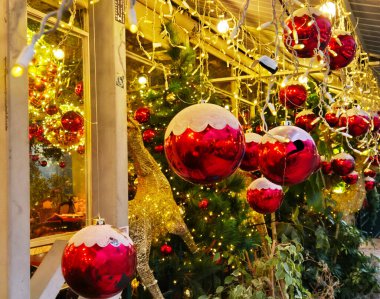 Kırmızı Noel süslerinin ve süslenmiş bir ağacın üzerinde parlayan sarı ışıkların yakın görüntüsü sıcak ve şenlikli bir tatil atmosferi yaratıyor..