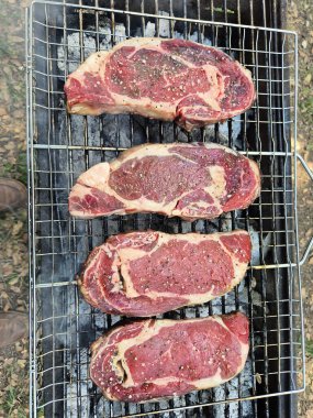 Sıcak ızgarada pişmiş çiğ bifteklerin yakın plan görüntüsü. Altında görünür kömürler var. Güneşli orman ortamında pişirmeye hazır..