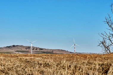 Rüzgâr türbinleri kurak ve güneşli bir günde açık mavi gökyüzünün altında yenilenebilir enerji üretir..