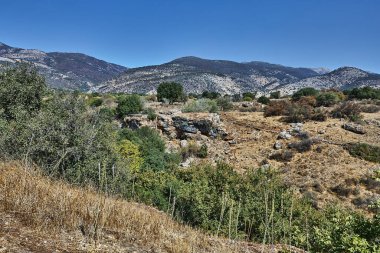 Nadir bitki örtüsü ve kayalık oluşumlarıyla çorak vadi uzak dağ zirvelerinin ve açık mavi gökyüzünün altında yer alır..