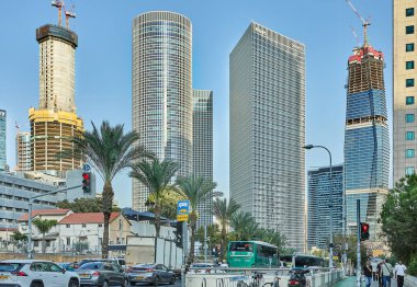 Tel Aviv, İsrail - 19 Kasım 2025: Trafik ve palmiye ağaçları ön plandaki işlek caddeleri doldururken, pencereleri ızgara pencereli uzun gökdelenler Tel Aviv siluetine hakim oluyor.
