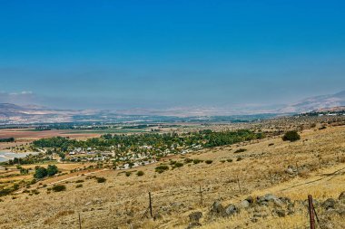 Kırsal köy yeşil tarlaların yanında, kuru tepelerle çevrili, açık görüş mesafesi olan sisli mavi bir gökyüzünün altında..
