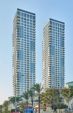 Tel Aviv, İsrail - 19 Kasım 2025: İkiz yerleşim yeri gökdelenleri palmiye ağaçları ve trafiğin üzerinde yükseliyor, modern bir şehir manzarasında güneş ışığını yansıtıyor.