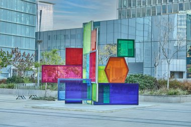 Renkli yarı saydam panellerden yapılmış canlı geometrik heykel aynalı ofis binalarıyla çevrili iş alanı meydanında duruyor..