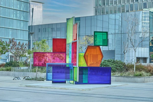 Renkli yarı saydam panellerden yapılmış canlı geometrik heykel aynalı ofis binalarıyla çevrili iş alanı meydanında duruyor..