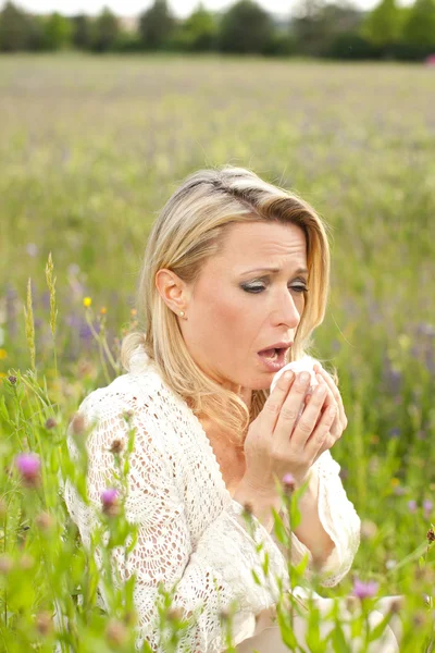 Attraktive Frau auf einem Blumenfeld mit allergischen Symptomen — Stockfoto