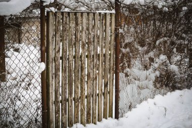 Kışın karlı havada tel örgülü küçük tahta giriş kapısı.
